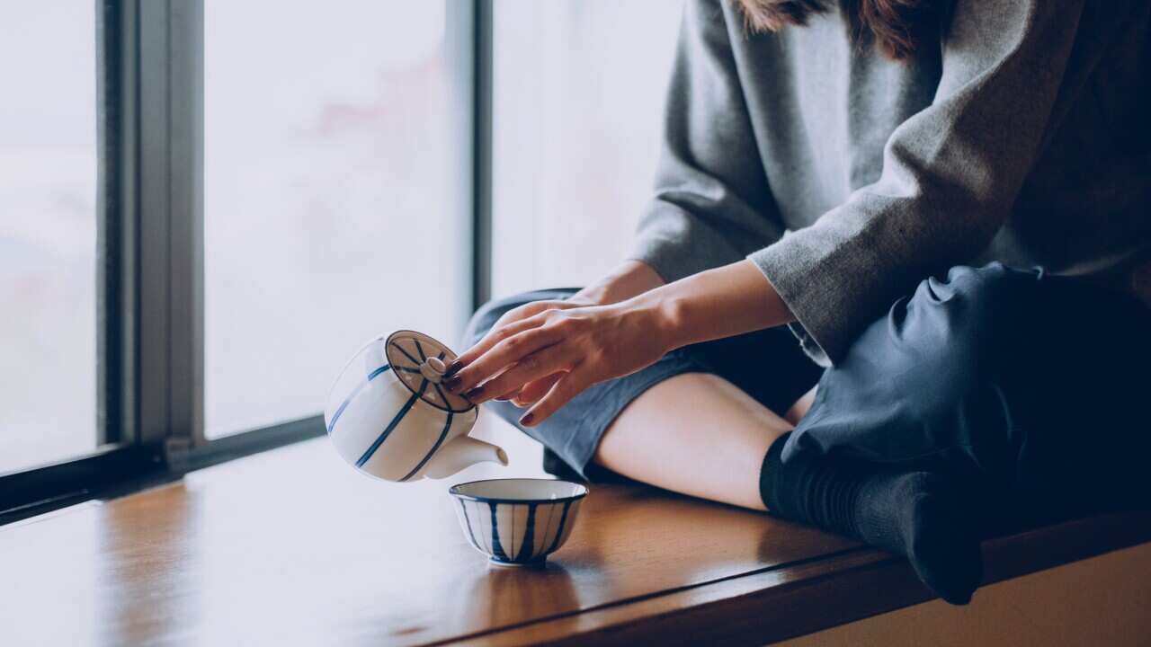 Woman sitting on the windowsill and pouring a cup of tea