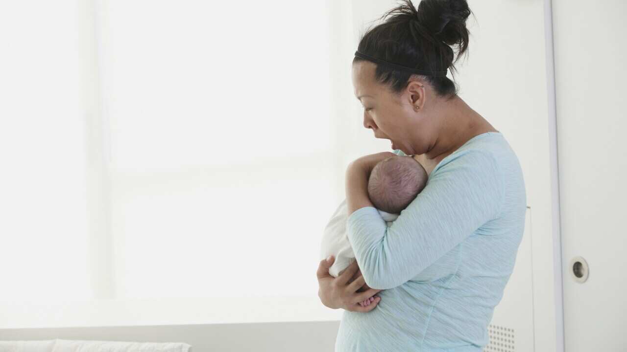 Yawning Chinese mother holding newborn