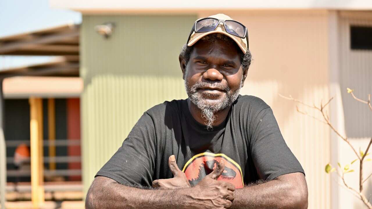 Ron Poantumilui, Indigenous man wearing black shirt and hat leaning against a sign