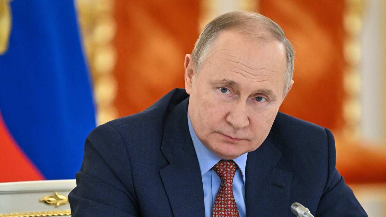 Russian President Vladimir Putin sits at a desk in front of a microphone.