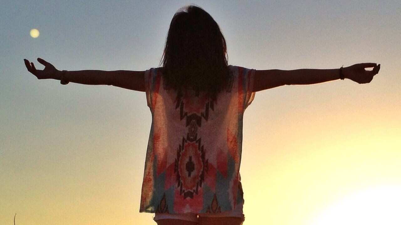 Rear view of young woman with arms outstretched enjoying sunset