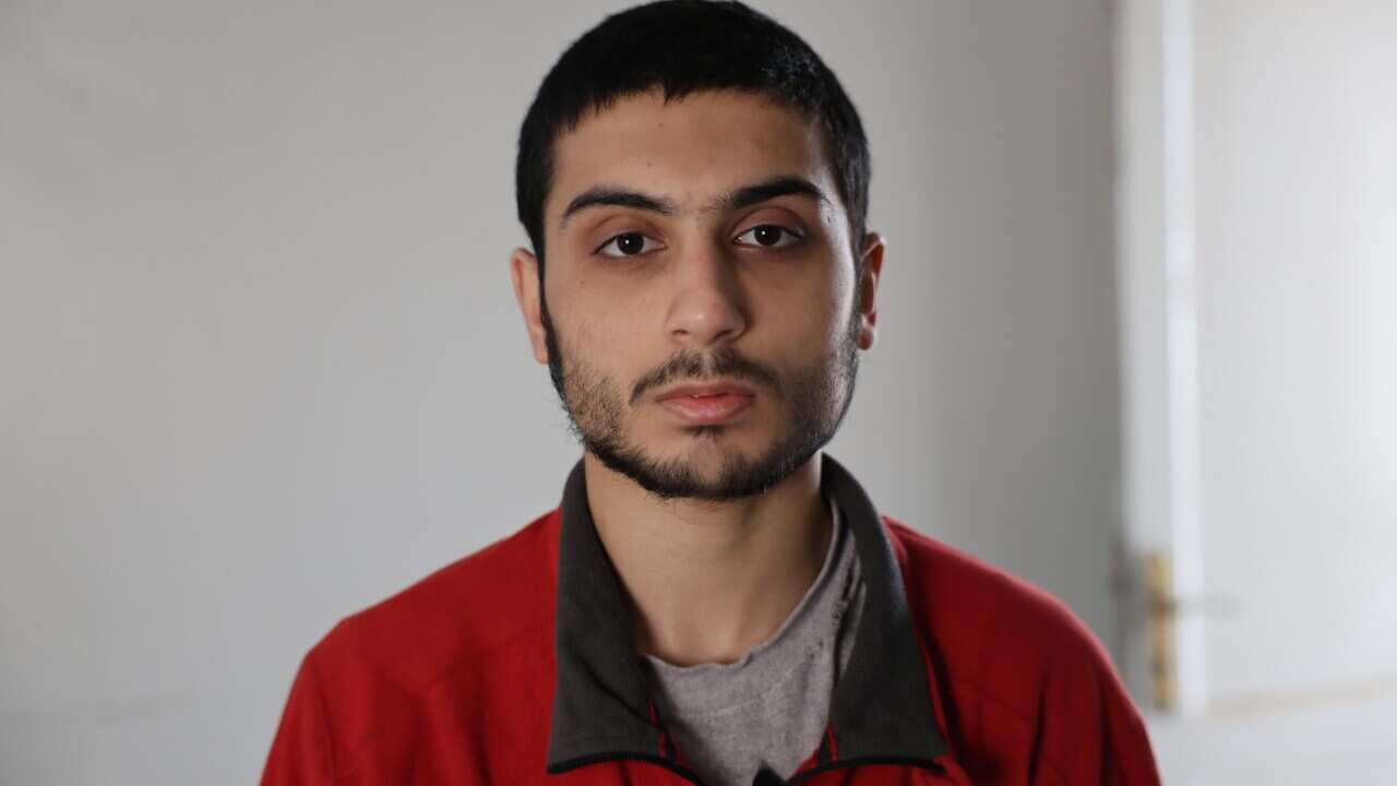 A head-and-shoulders shot of a young man in a red fleece looking at the camera with a serious expression.