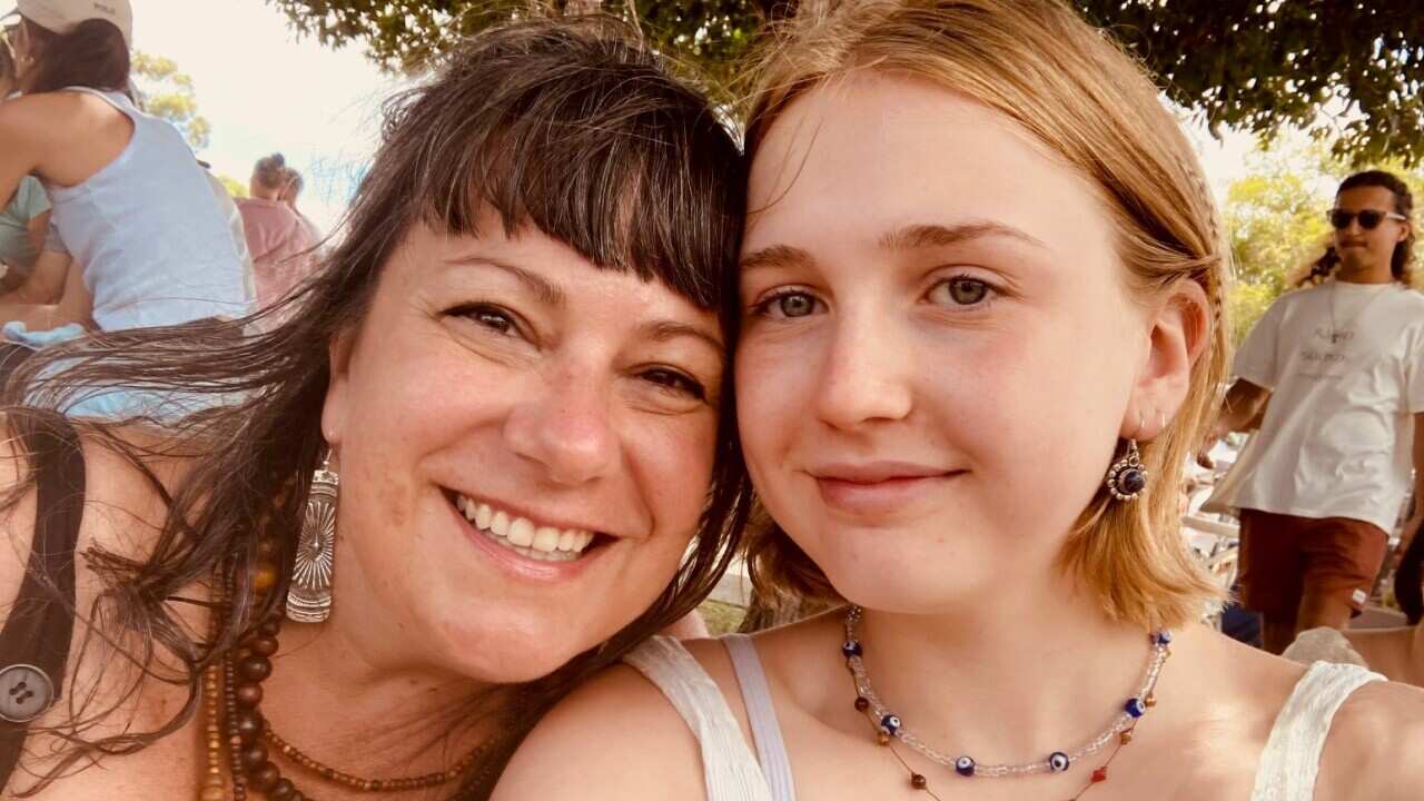 An older woman smiles as she poses with her teenage daughter