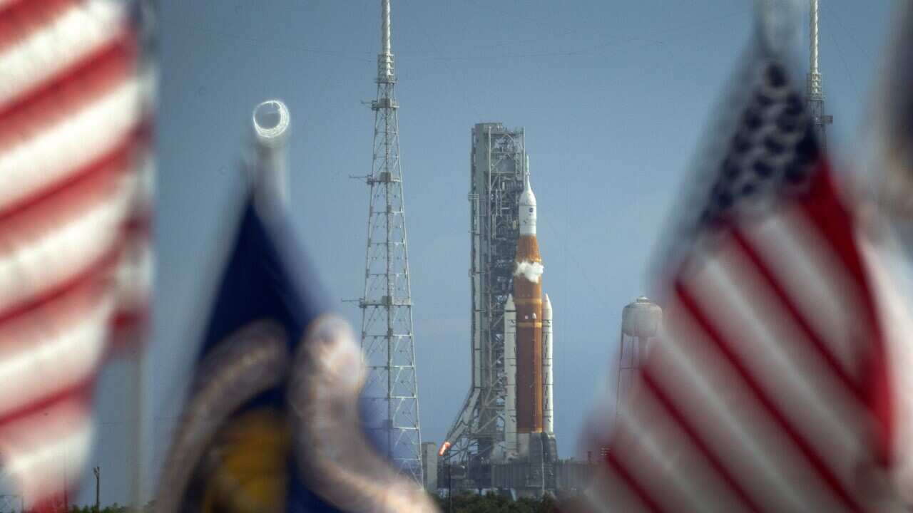 The Space Launch System rocket with an Orion capsule is seen behind American flags. 