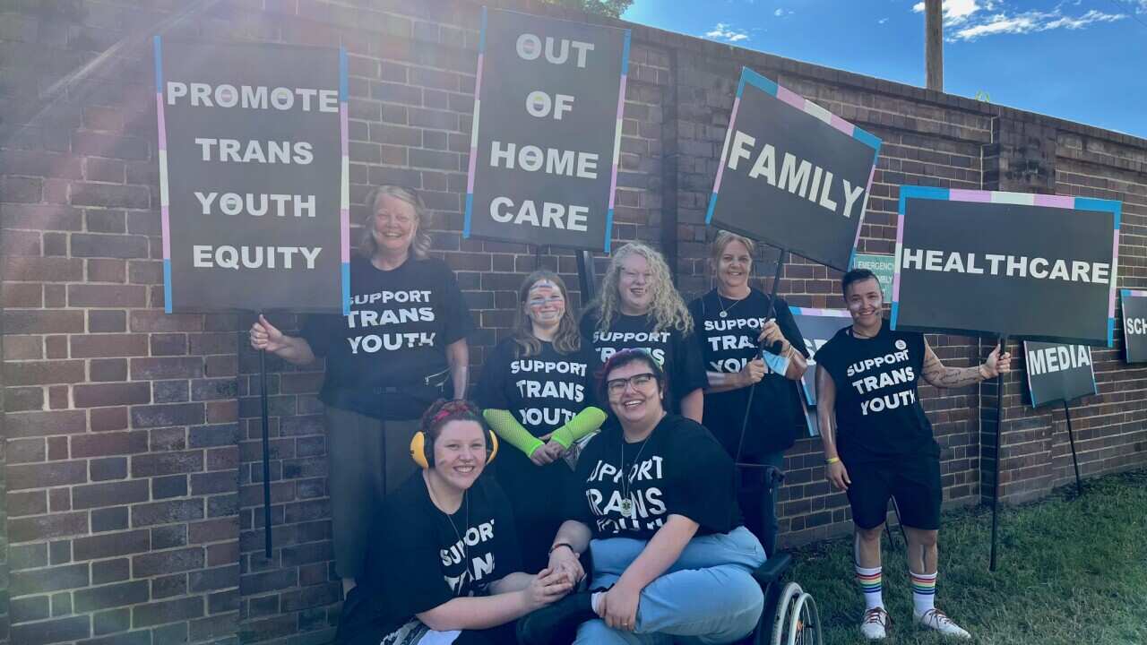 Members of the Trans Youth Equity smiling and wearing black outfits saying "support trans youth" at Mardi Gras 2022