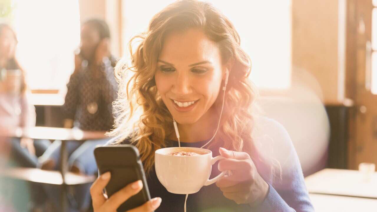 Woman with headphones drinking cappuccino and video chatting in cafe