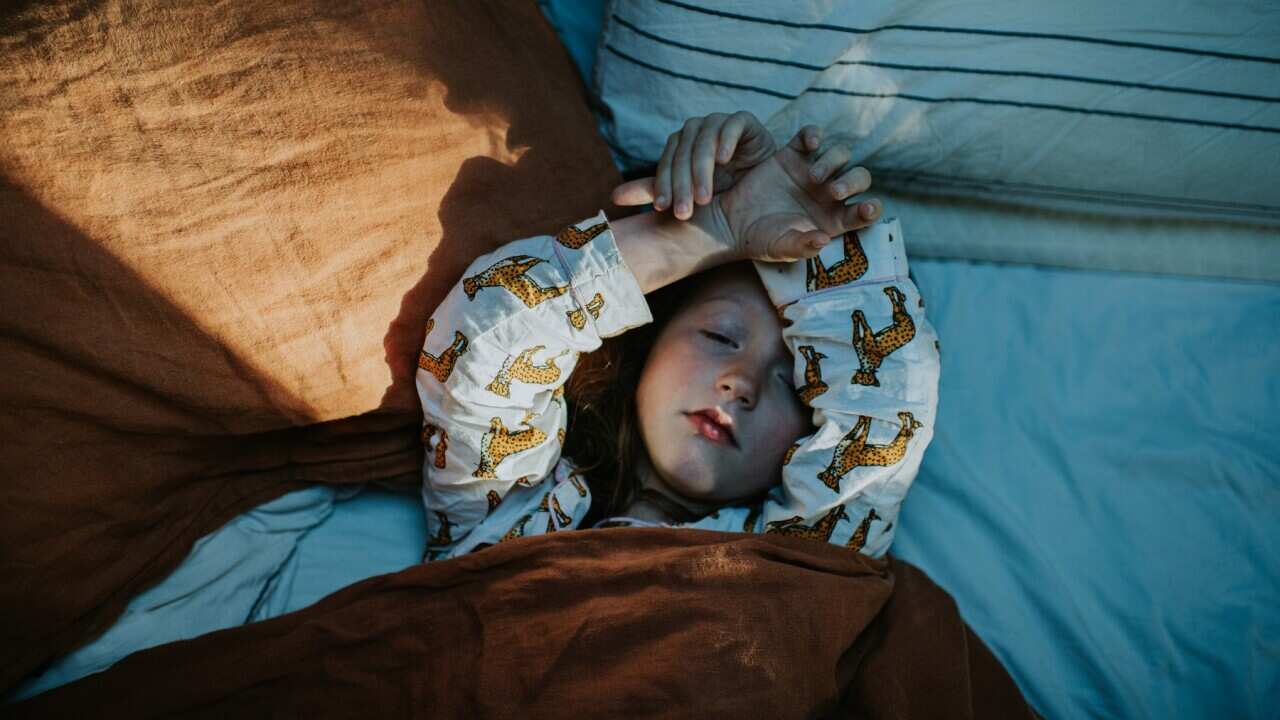 A little girl lies in bed, wrapped in a cozy duvet