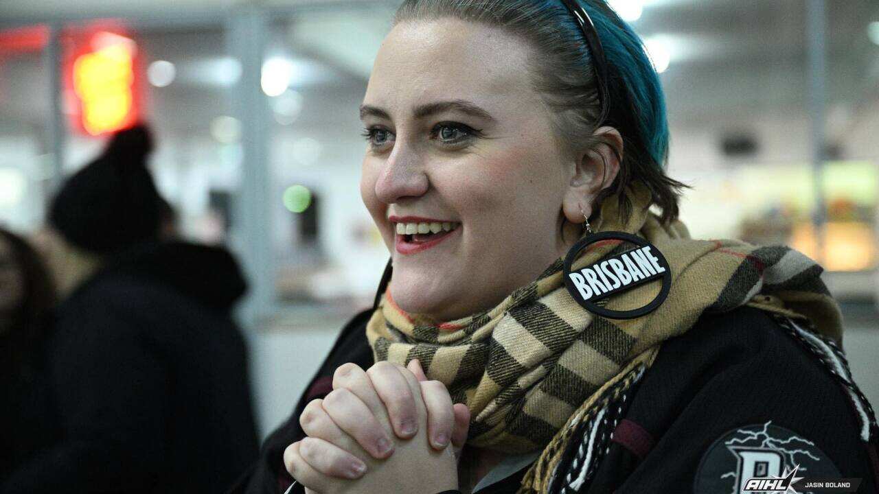 A young woman wearing a scarf, smiling and clasping her hands