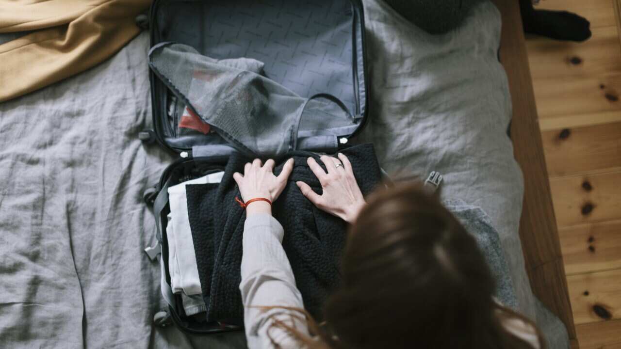 Woman packing a suitcase on her bed.