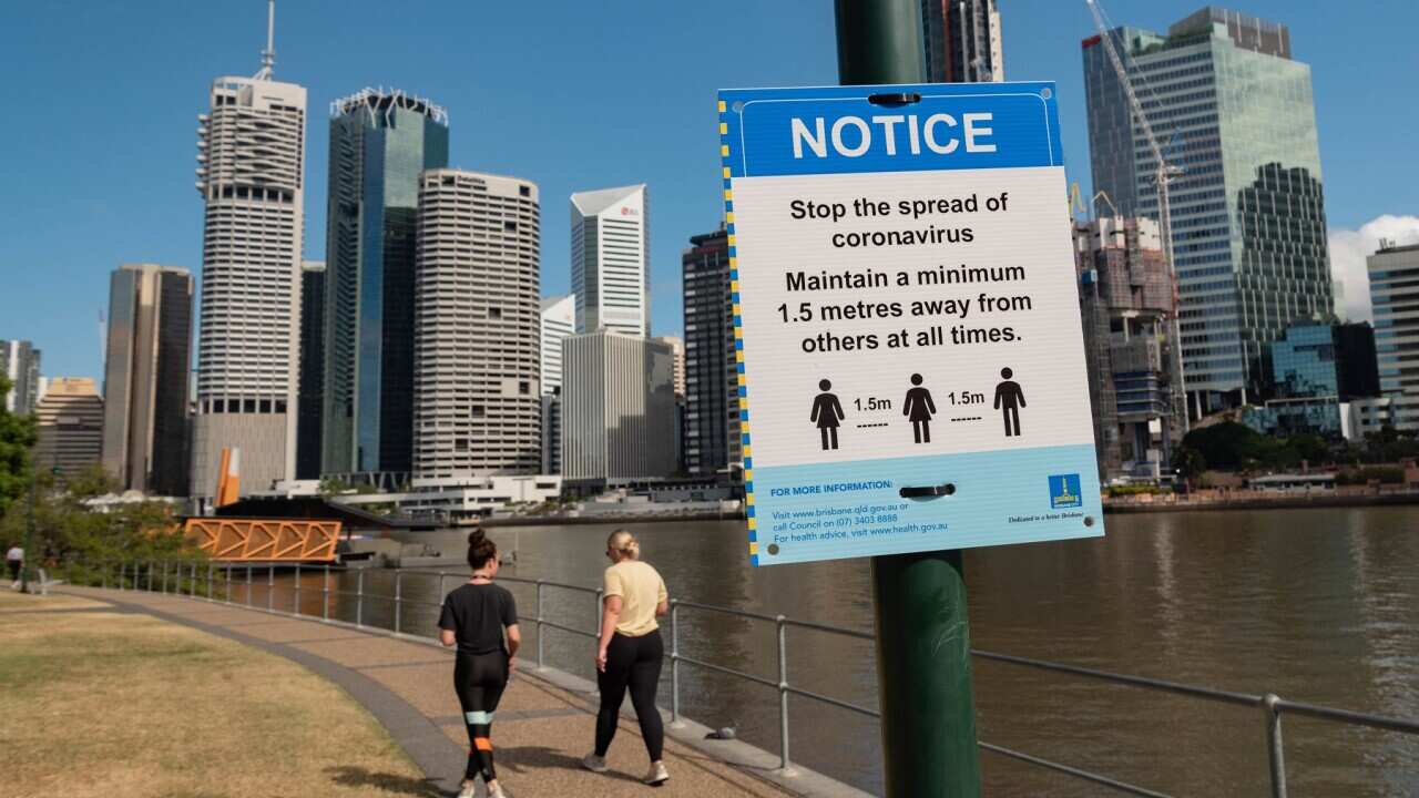 Two ladies walk past a sign warning the public about social distancing amid Coronavirus pandemic.
