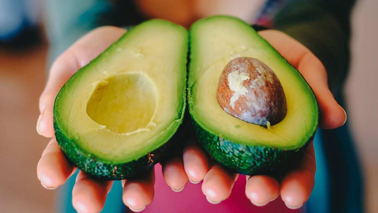 Woman holding out halved avocado