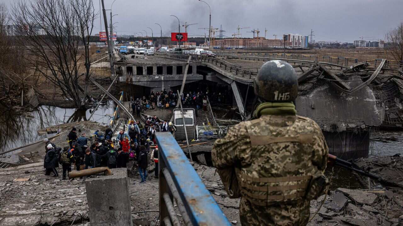 A Ukrainian serviceman looks on as evacuees cross a destroyed bridge as they flee the city of Irpin, northwest of Kyiv.