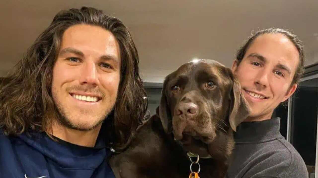 Two men with brown hair posing for a photo with a brown dog.