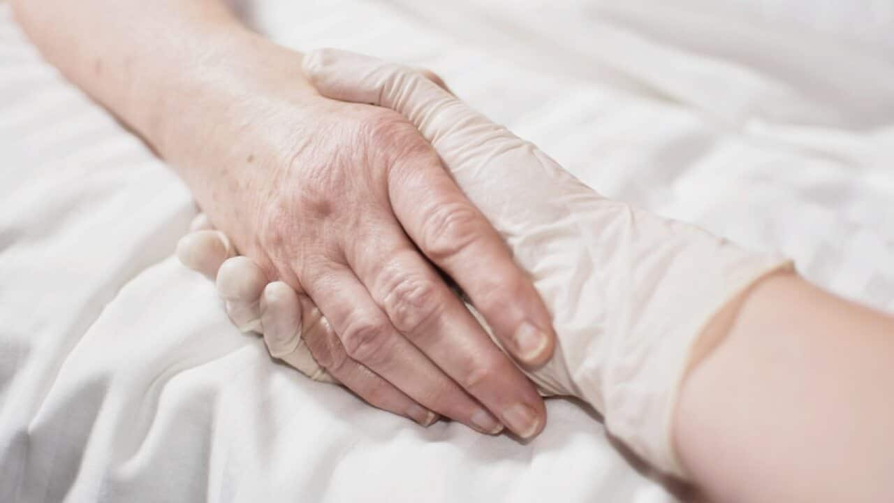 Image of a health worker's hand wearing a glove holding a patient's hand