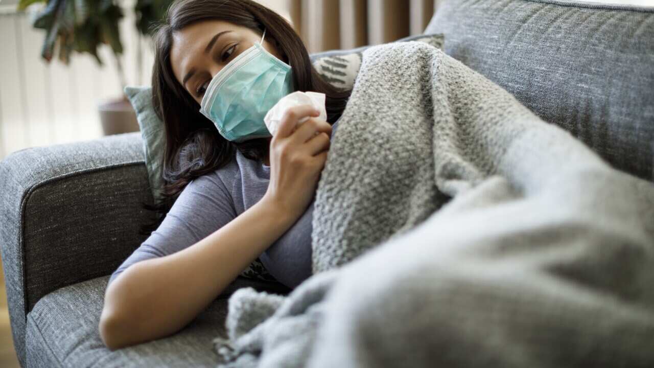 A sick woman wearing a face mask lying in bed