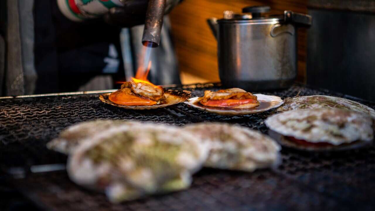 Vendor cooking scallops on steel grill in a market in Japan