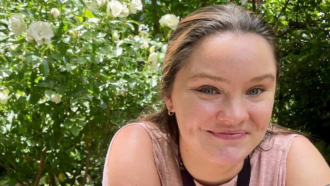 Close up of a young woman half smiling with rose bushes in the background.