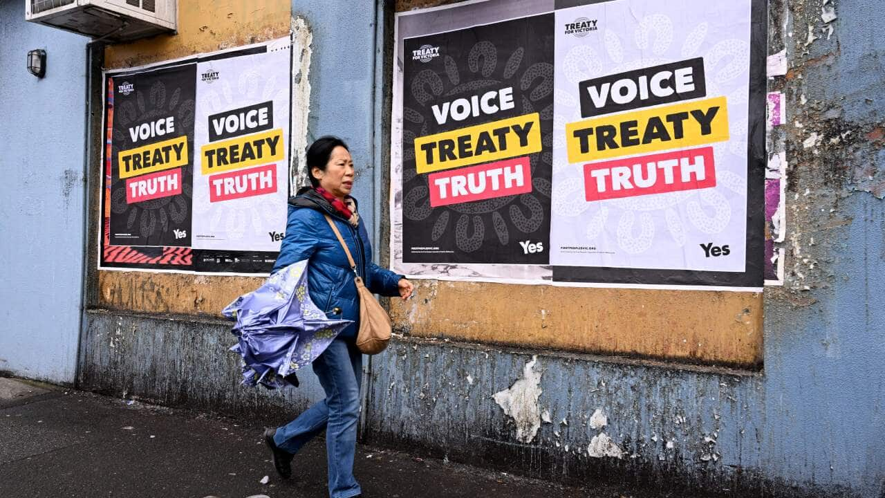 A woman with a bag and umbrella walks past posters on a wall.