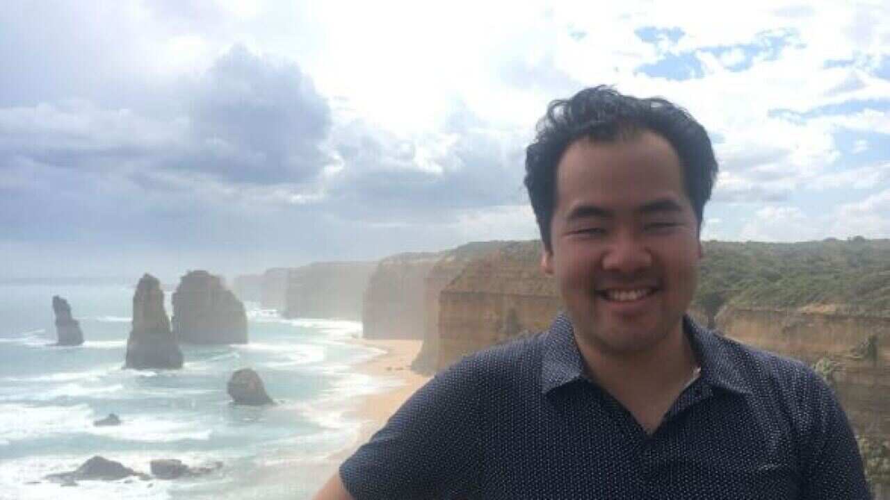 A man smiles as he poses in front of a beach