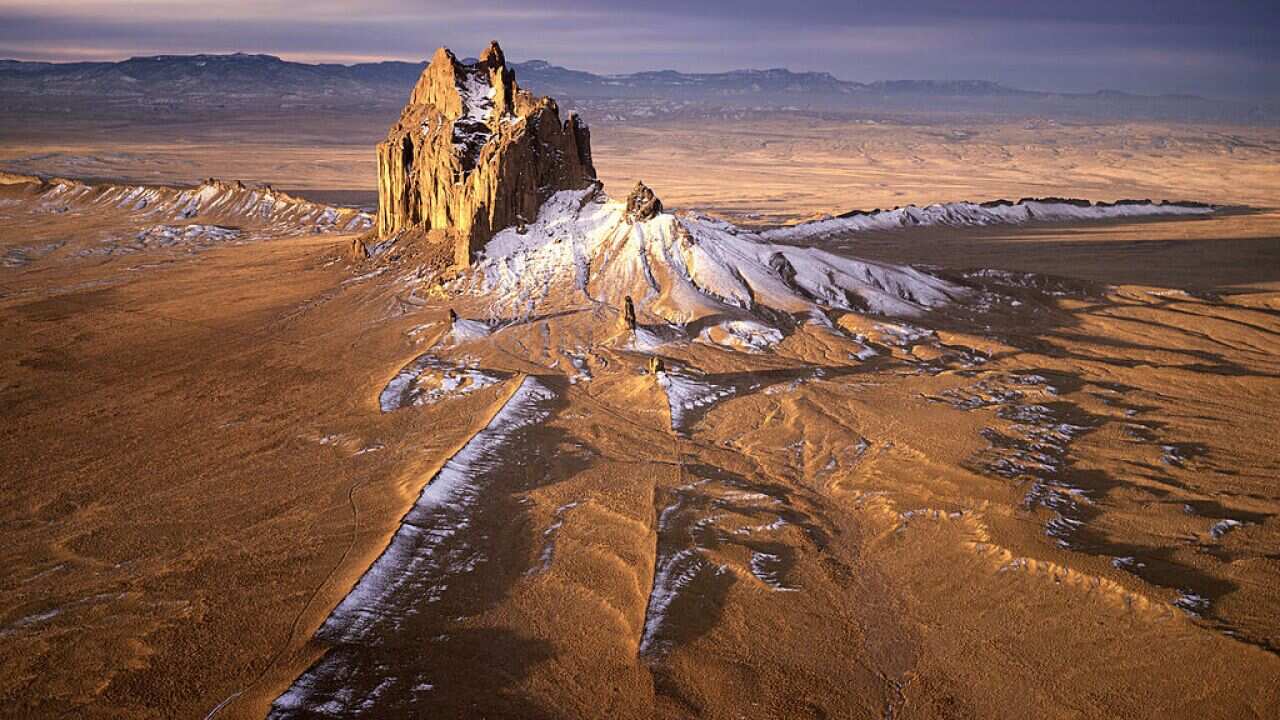 Aerial view of Shiprock at sunrise, a monumental landform sacred to the Navajo people, graced by a winter snowfall This is the American Southwest's most famous volcanic neck, also known as a volcanic plug, which rises 1,800 feet above the valley flo