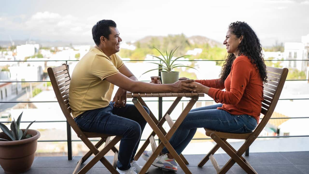 Couple smiling at each other while drinking coffee on balcony