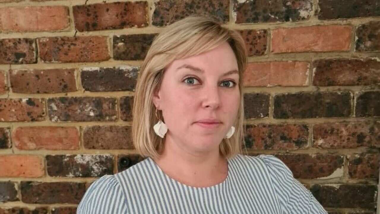 A blonde woman with earrings standing in front of a brick wall.