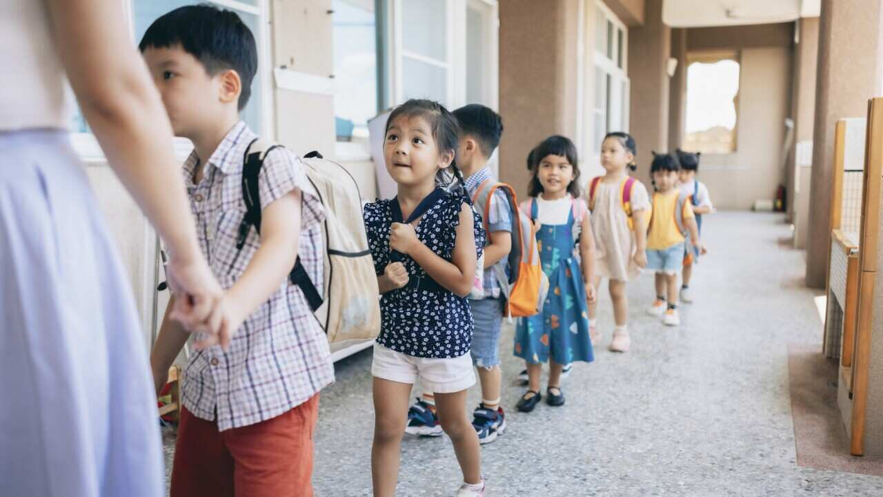 Preschool teacher guiding and arranging students waiting in line entering classroom