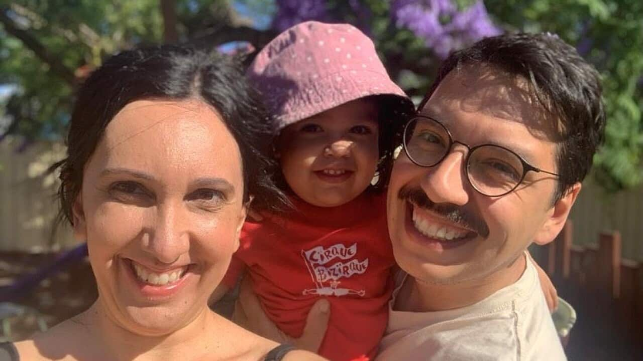 Parents holding toddler daughter, standing in the garden and smiling at camera.