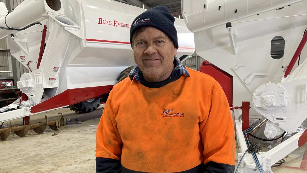 A man wearing a beanie and jumper standing in a factory with grain carts behind him.