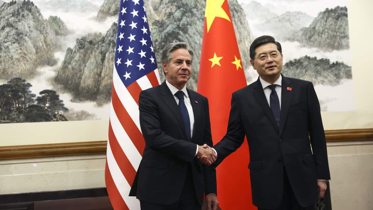 Two men shake hands in front of their respective country's flags.