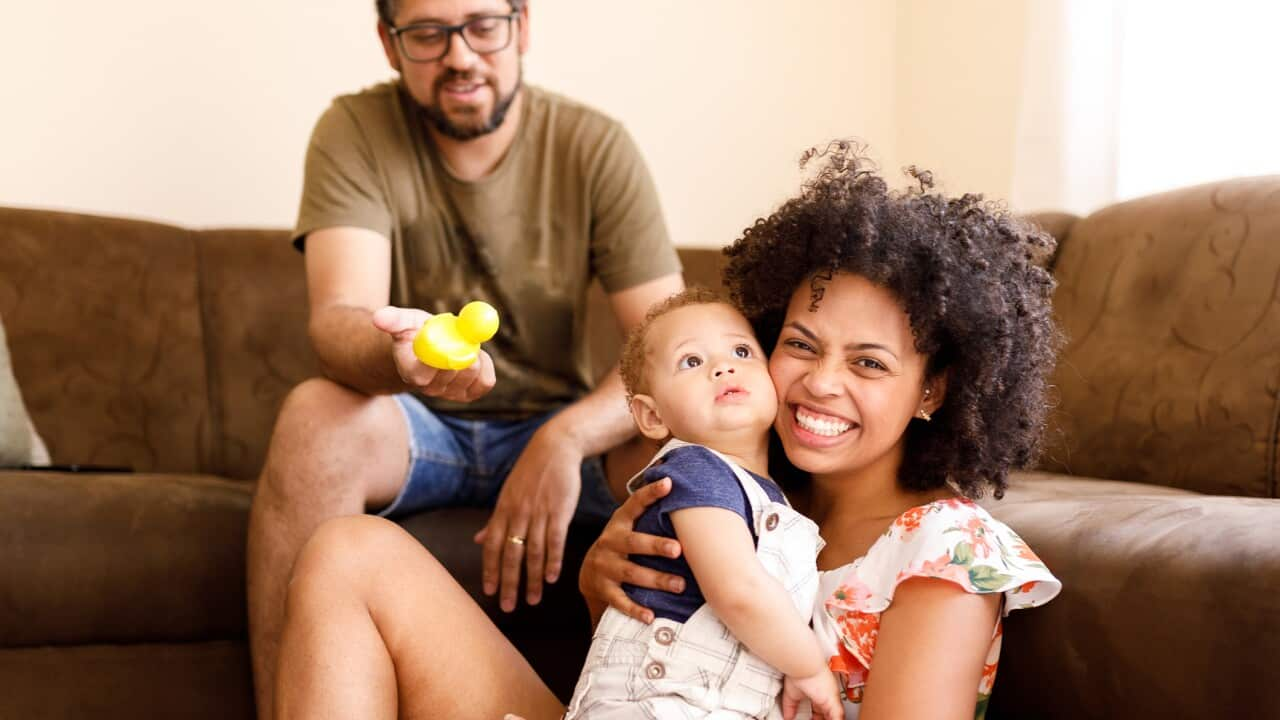 Father, baby and mother playing on the sofa at home.