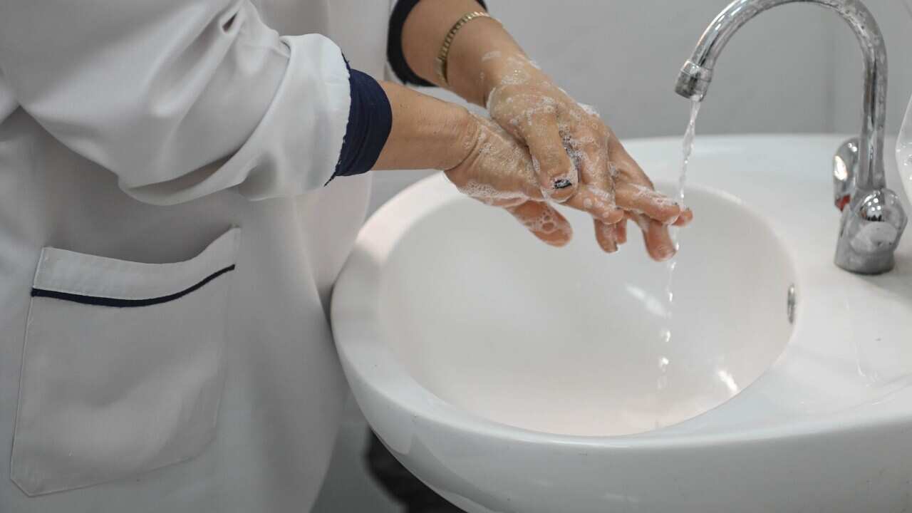 A nurse washes her hands with soap at a wash basin. 