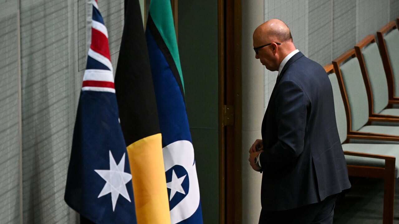 A man walks by the Australian, Aboriginal and Torres Straits flags.