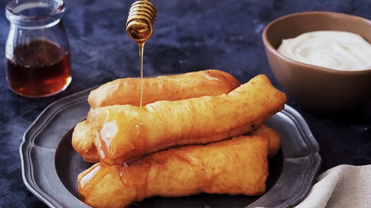 Bosnian fried pastry being drizzled with honey