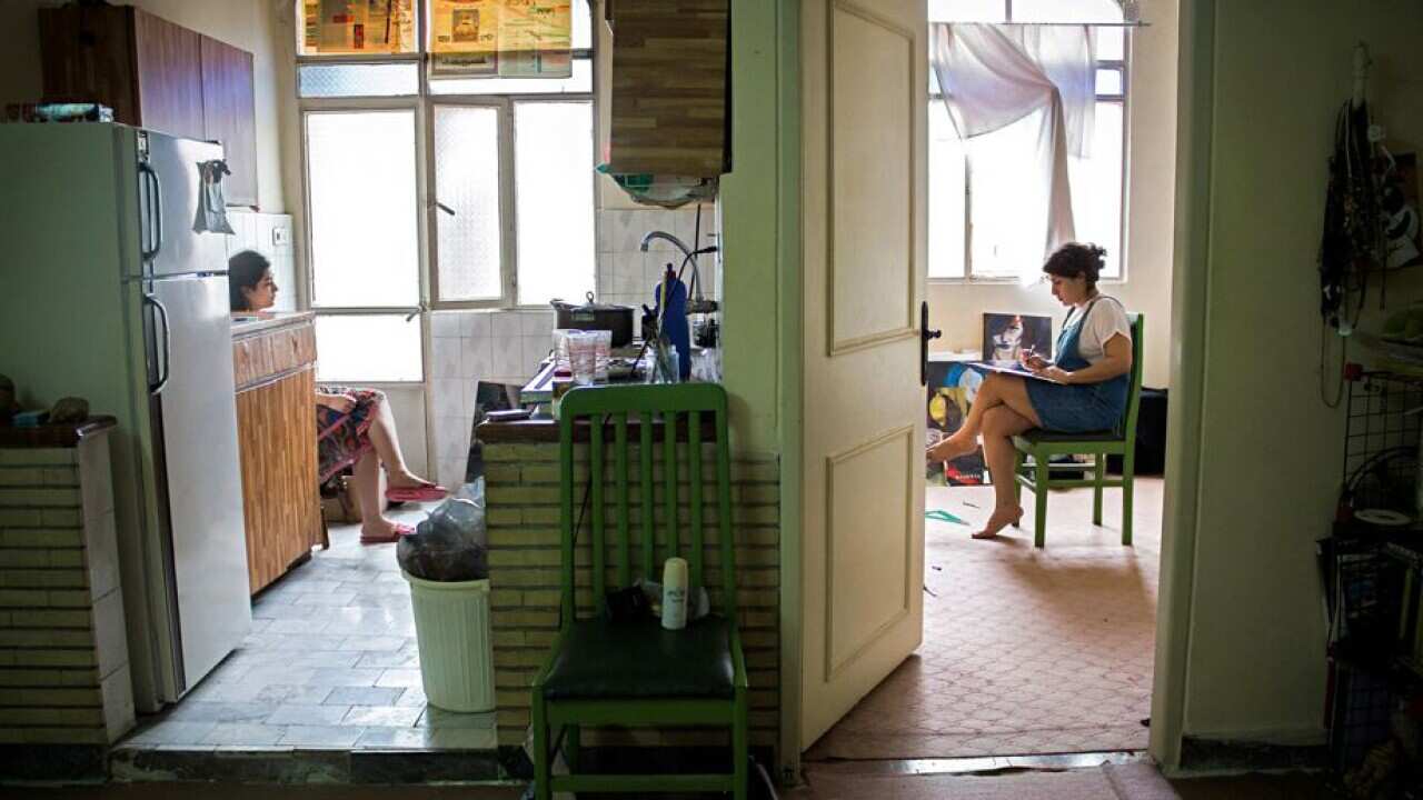 Yasmin paints her bedroom while roommate Negar sits in the kitchen.