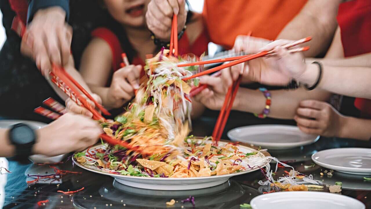 an asian chinese family celebrating chinese new year's eve with traditional food Lou sang (raw fish dishes) during reunion dinner