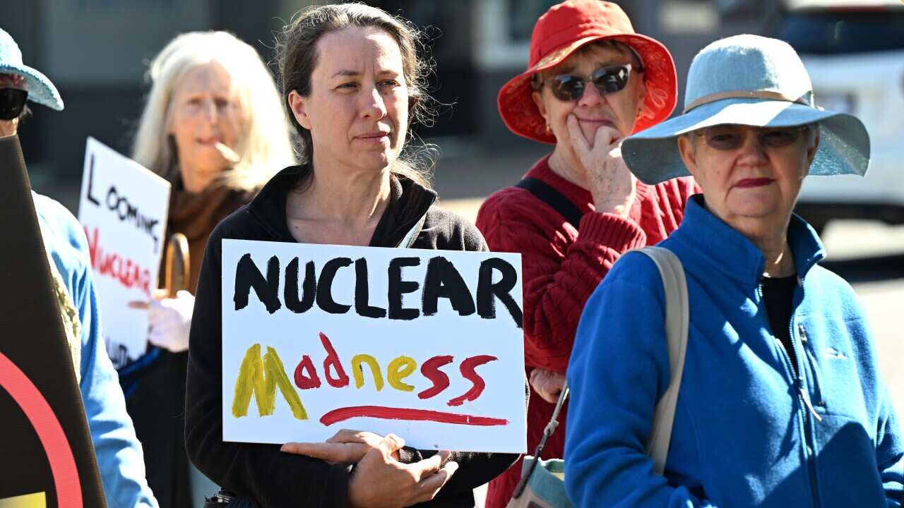 A woman holds a placard saying "nuclear madness" with other protesters around her.