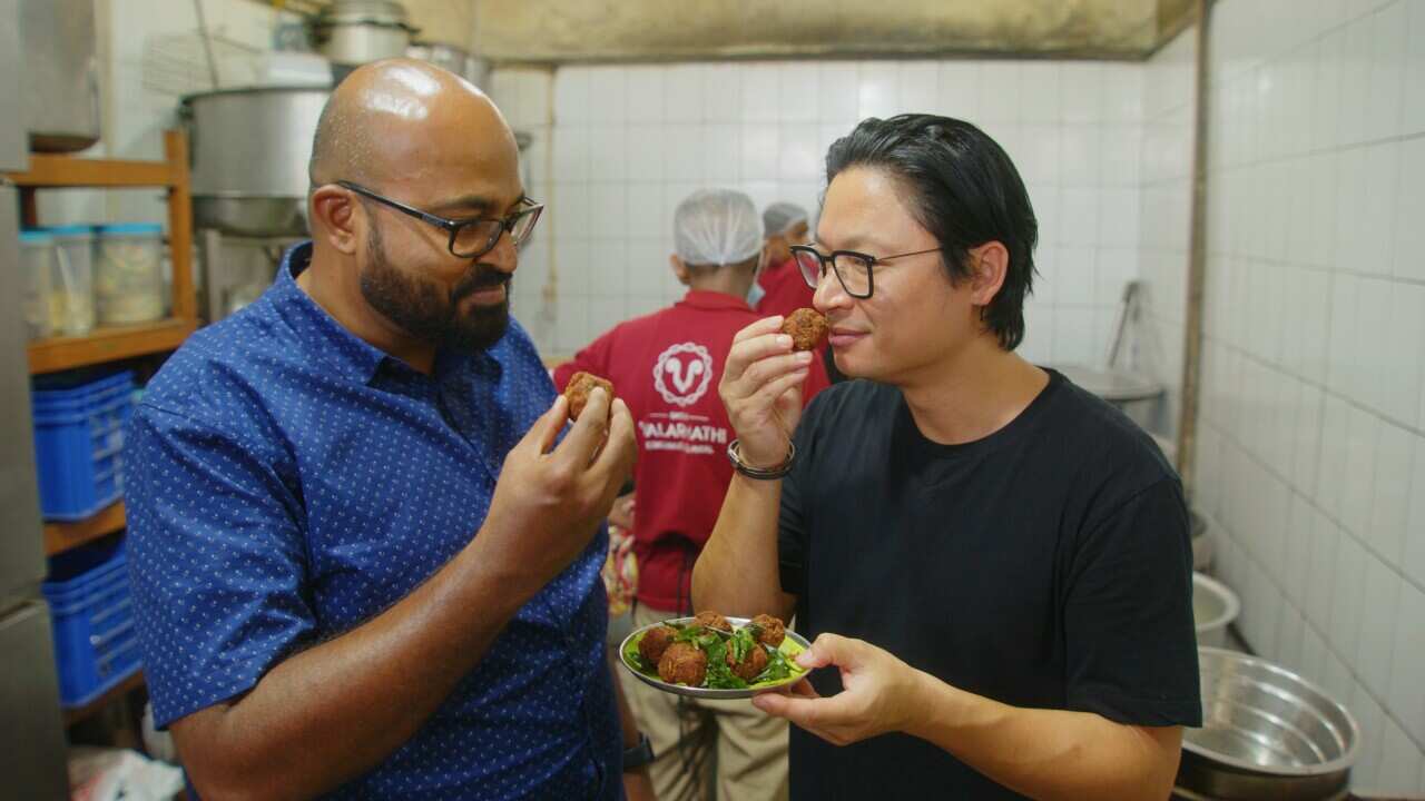 Chef Luke Nguyen (right) smells food with another man in a kitchen.