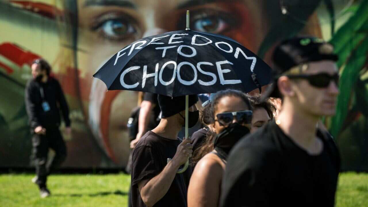 Protesters in Melbourne rally against COVID-19 restrictions. One holds a black umbrella with white writing on it reading 'Freedom to Choose.'