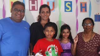 Family members standing together in front of  white wall with colourful streamer and signs that spell out "KHUSH".