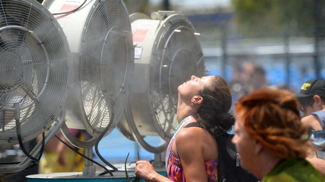 A woman cools herself down in front of a fan.