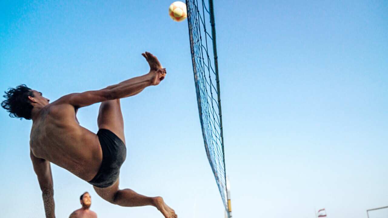 Brazilian man jumping and kicking ball on beach in Brazil