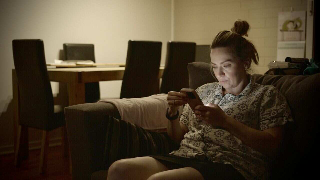 A woman dressed in her pyjamas looks at her phone in a darkened room