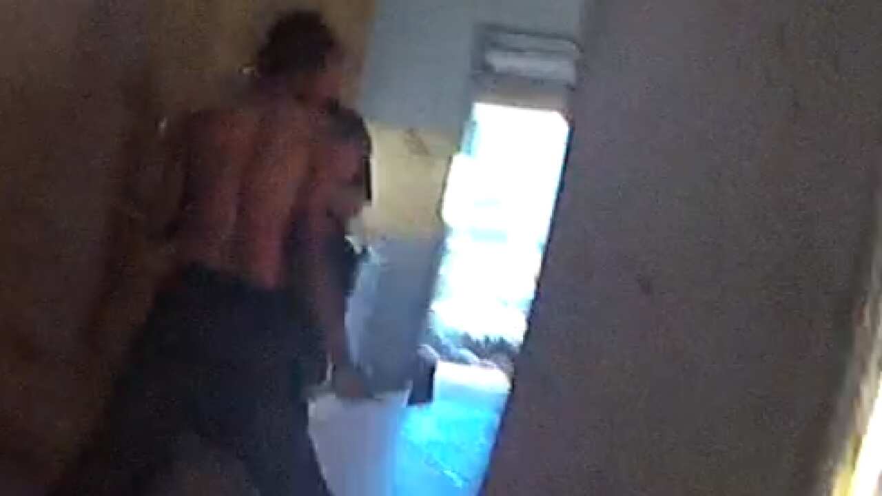 Kumanjayi walker seen from the back holding an axe in his hand while pushing past an officer. 