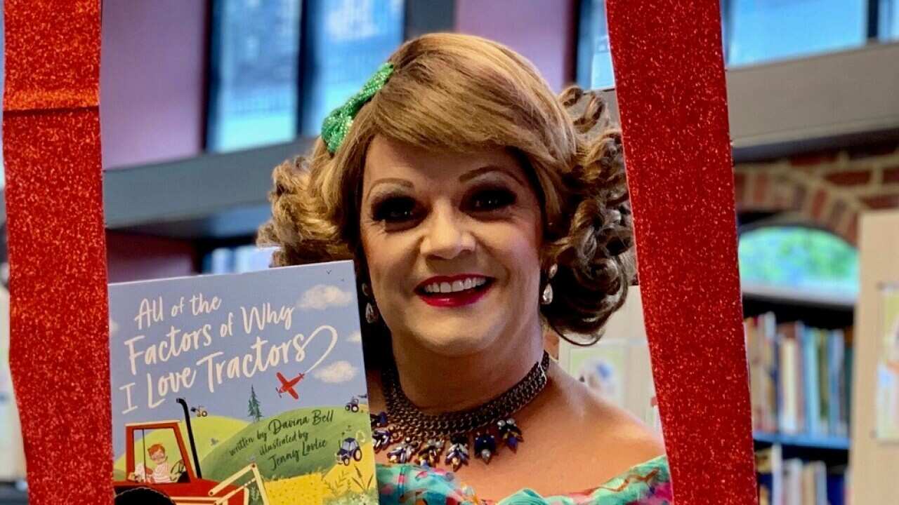 Drag queen Dolly holds up a children's book. 