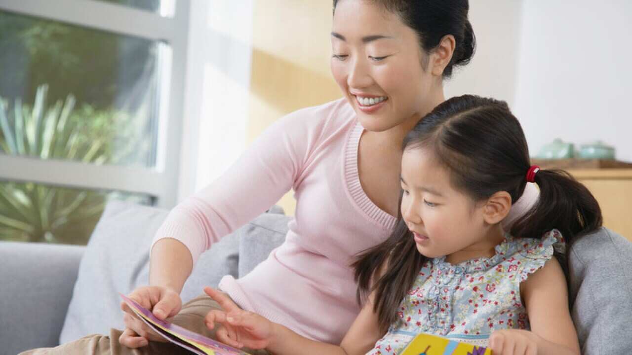 Mother sitting with daughter on sofa reading a book