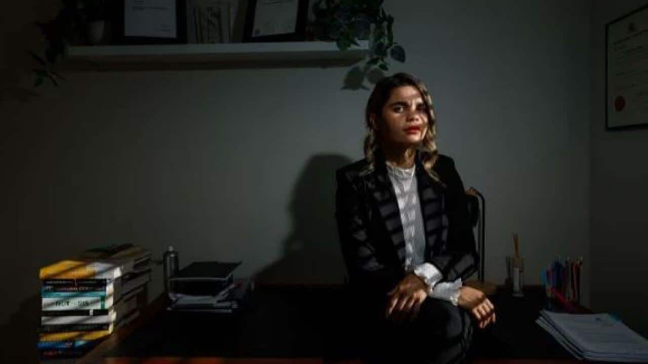 Dark picture of a young woman in a suit sitting in an office.