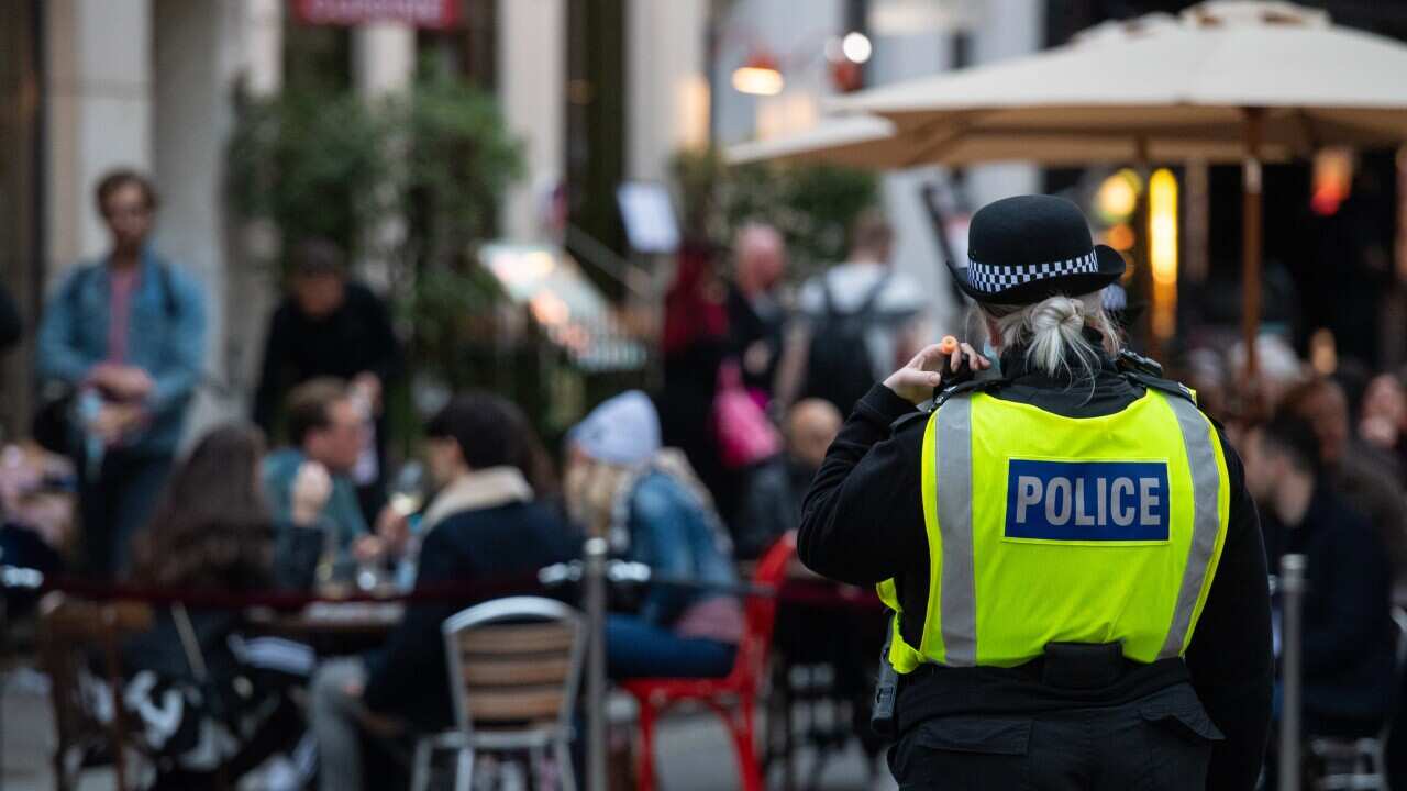 Police monitor people seated outside bars and restaurants in Soho, London, on the first day after the city was put into Tier 2 restrictions