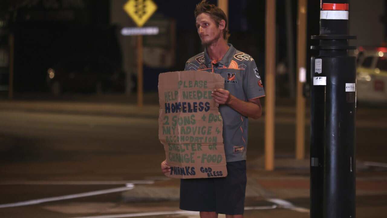 A middle-aged man holding up cardboard at a busy intersection, pleading for spare change