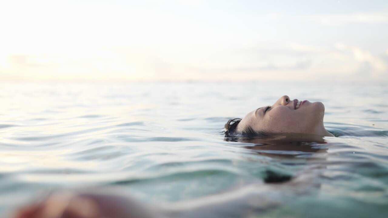 Woman floating in sea, smiling, profile